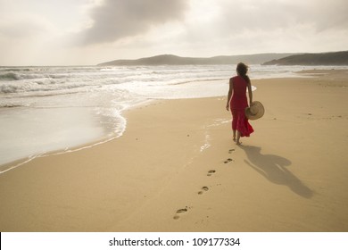 Mujer joven camina en una playa salvaje vacía hacia vigas de luz celestiales cayendo del cielo