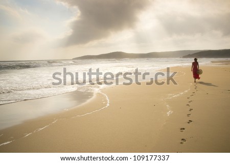 Young woman walk on an empty wild beach towards celestial beams of light falling from the sky