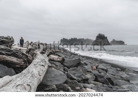 Young woman walking among rocks and driftwood on Rialto Beach in Olympic National Park.