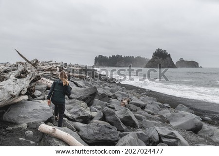 Young woman walking among rocks and driftwood on Rialto Beach in Olympic National Park.
