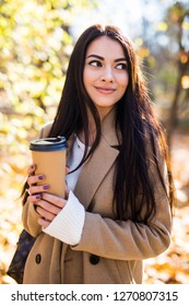 Young woman walking in the autumn city street and drinking take away coffee in paper cup.