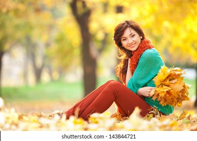 Young Woman Walking In The Autumn Park. Beauty Nature Scene With Colorful Foliage Background, Yellow Trees And Leaves At Fall Season. Autumn Outdoor Lifestyle. Happy Smiling Woman Relax On Fall Leaves