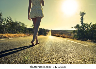 Young Woman Walking Barefoot On A Long Deserted Road