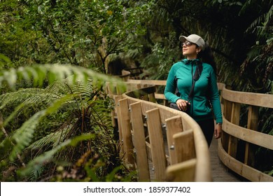 Young woman walking by wooden bridge surrounded by new zealand native vegetation.