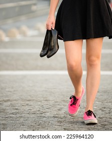 Young woman  walking down street in sneakers and high heels shoes holding in hands