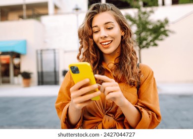Young woman walking down the street and using mobile phone. Business, technology, blogging, communication concept. - Powered by Shutterstock