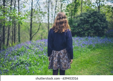 A Young Woman Is Walking In A Forest With Bluebells