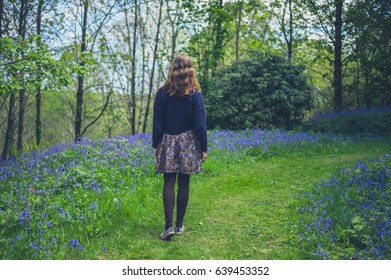 A Young Woman Is Walking In A Forest With Bluebells