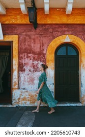 Young Woman Walking Next To An Old Building In Italy, Blonde Girl With A Colorful Pink House In Sicily, Vertical View