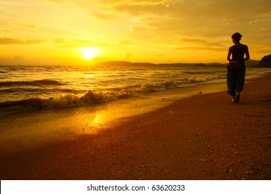 Young Woman Walking On Beach Under Sunset Light