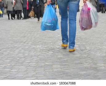 Young woman walking on a busy city street and holding colored plastic shopping bags with various groceries, high cost of living in the city