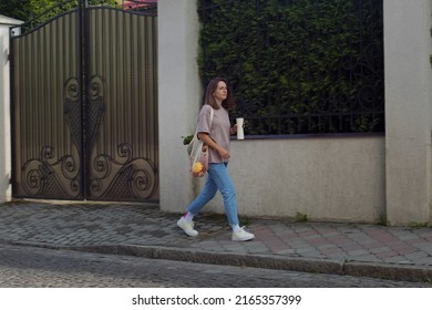 Young Woman Walking On City Street With A Reusable String Eco Bag Full Of Groceries And Drinks From Reusable Metal Cup. Young Girl Going Home After Shopping With String Mesh Bag With Vegetables. Consc