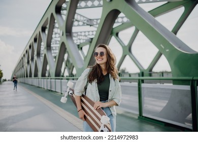 Young woman walking on city bridge with skateboard. Youth culture and commuting concept. - Powered by Shutterstock