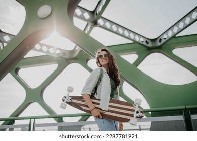 Young woman walking on city bridge with skateboard. Youth culture and commuting concept. - Powered by Shutterstock