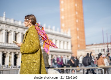 Young woman walking on famous saint Marks square in Venice. Concept of visiting italian landmarks and travel. Woman wearing coat and shawl in italian style
