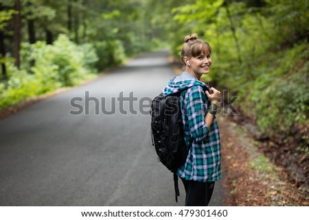 young woman walking on a road, traveling with her backpack alone on a mountain road listenting music