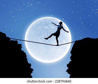 Young woman walking on rope above gap at night