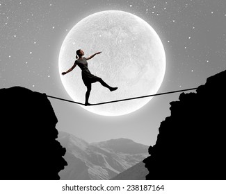 Young woman walking on rope above gap at night