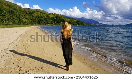 Young woman walking on sand in empty beach at sunset in Ilhabela Island, Brazil