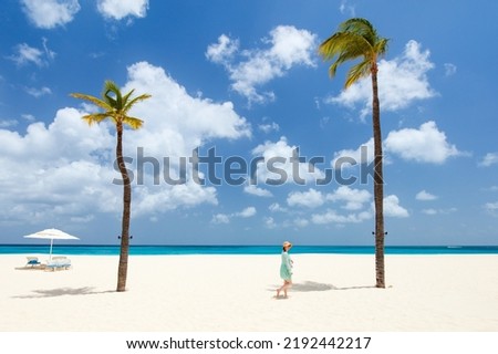Young woman walking on white sand tropical beach surrounded by turquoise ocean water on island of Aruba