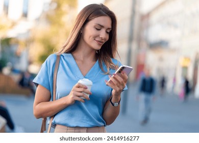 Young woman walking outdoors, holding takeaway coffee cup, using mobile phone - Powered by Shutterstock