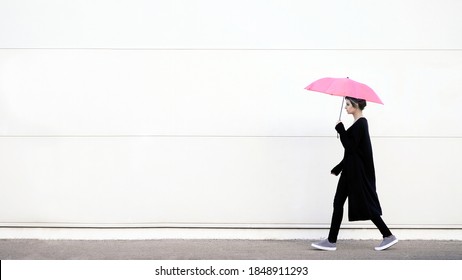 Young woman walking with pink umbrella in front of white wall - Powered by Shutterstock