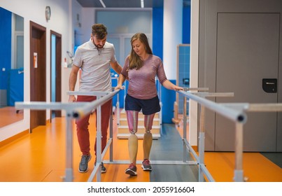 Young woman walking with prosthetic limbs being assisted by male physiotherapist  - Shutterstock ID 2055916604