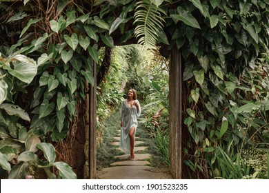 Young Woman Walking In Tropical Garden In Long Summer Dress, Greenery And Palm Trees Around, Enjoying Nature