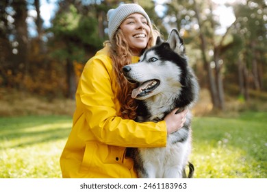 A young woman walks with her dog in the autumn forest. Husky dog.  Pet owner enjoys walking her dog outdoors. - Powered by Shutterstock