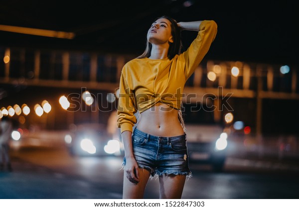 A young woman walks in the night city on the\
background of lights and the\
road.