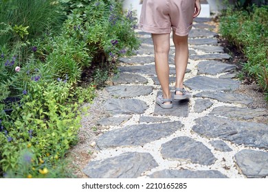 A Young Woman Walks On A Stone Path Decorated In The Garden.