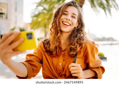 Young woman walks the streets and takes selfie using smartphone camera. Beautiful young photographer takes pictures for her travel blog. - Powered by Shutterstock