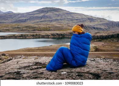 Young woman in warm blue sleeping bag , on the stones with northern mass, Iceland