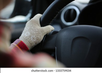 Young Woman In Warm Clothes Driving A Car In The Cold Season. One Hand In Female Beige Glove On Steering Wheel. Black Leather Interior. Driver's Shoulder In Blurry Foreground. Shallow Depth Of Field