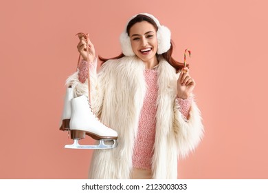 Young woman in warm clothes with ice skates and candy cane on pink background