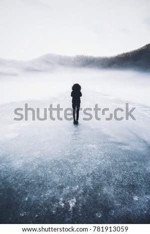 Young woman in warm clothing walking on cracked ice of a frozen lake 