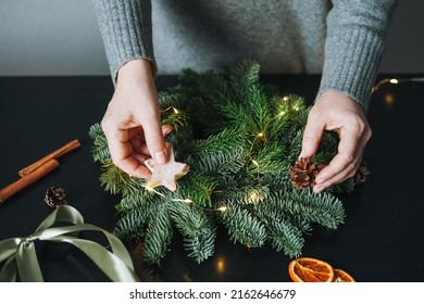 Young Woman In Warm Grey Knitted Dress Making Diy Fir Christmas Wreath In Hand On The Table At Home