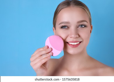 Young Woman Washing Face With Cleansing Brush On Light Blue Background. Cosmetic Product