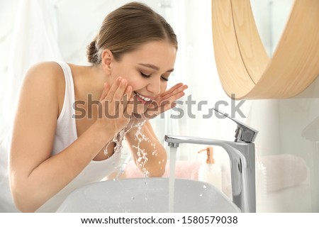 Young woman washing face with tap water in bathroom