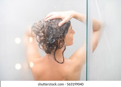 Young Woman Washing Hair With Shanpoo In The Shower. Back View