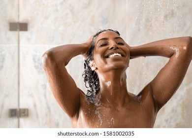 Young woman washing hair in shower at luxury spa. Woman washing her curly hair with shampoo and a lot of lather. Carefree black girl taking a long hot shower washing her hair in a modern bathroom.