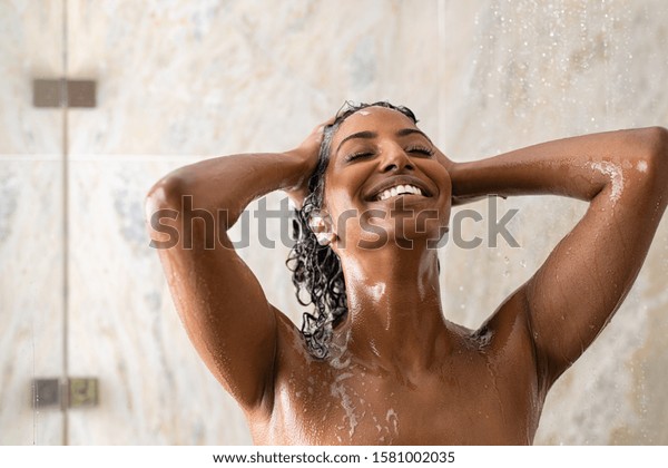 Young woman washing hair in shower at luxury\
spa. Woman washing her curly hair with shampoo and a lot of lather.\
Carefree black girl taking a long hot shower washing her hair in a\
modern bathroom.