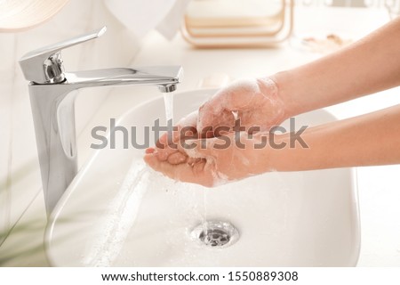 Young woman washing hands with soap over sink in bathroom, closeup