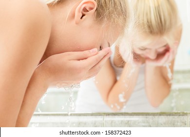 Young woman washing her face with clean water in bathroom