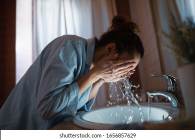 Young Woman Washing Her Face In Bathroom Sink. 