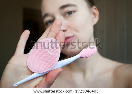 Young woman washing her face with a brush. Special silicone brush for cleansing pores. A young blonde shows a  silicone brush for the face at the camera. Selective focus. 