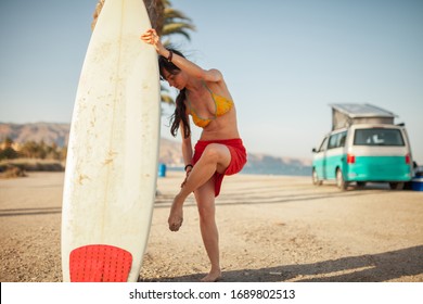 Young woman washing her feet in the beach with her surfboard - Powered by Shutterstock