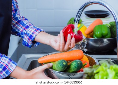 Young woman washing lettuce and apples to remove pesticides before cooking in kitchen. Fruit and vegetables washing concept.