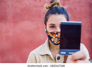 Young woman watching an instax photo with a flowers mask with a red wall on the background.