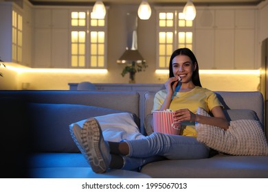 Young Woman Watching Movie With Popcorn On Sofa At Night, Space For Text